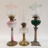An oil lamp, with a pink glass well, 70 cm, another with a green glass well, 71 cm, and another with