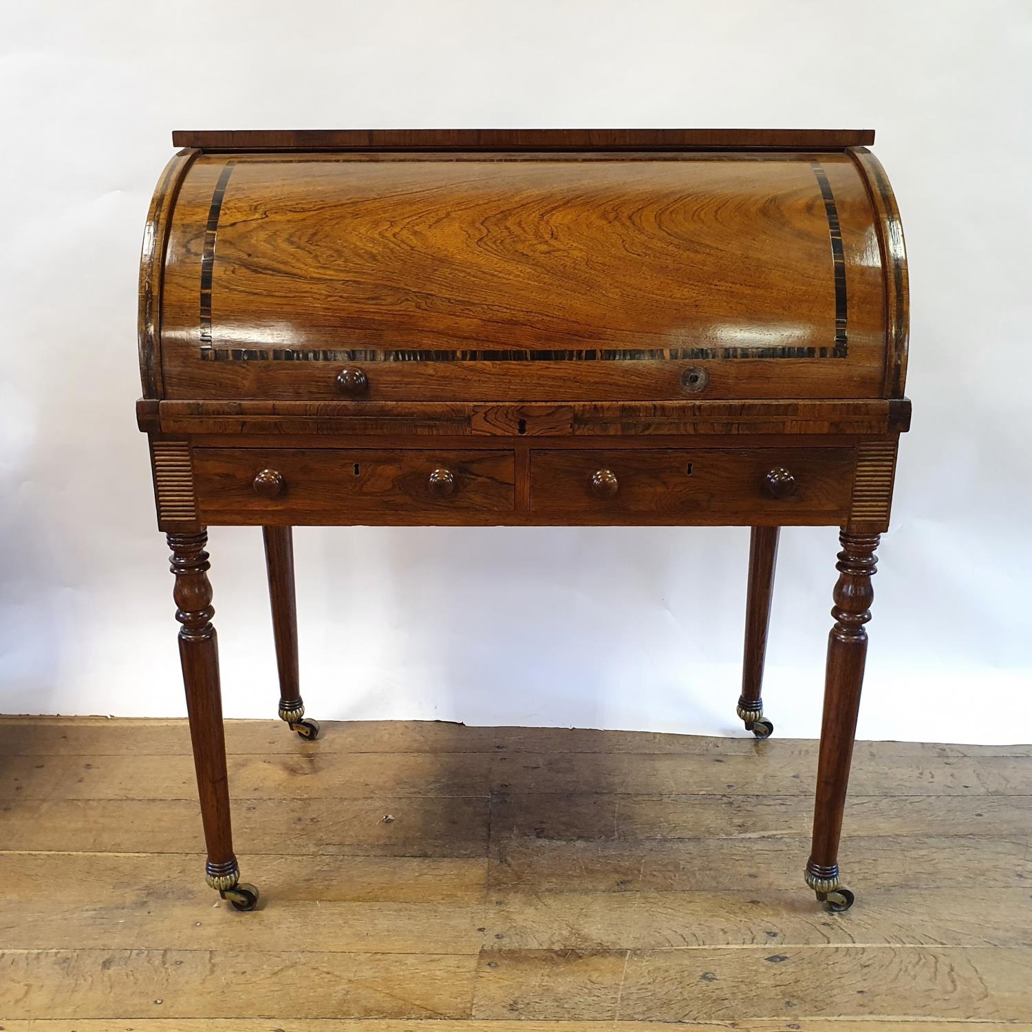 A late 19th century rosewood cylinder bureau, with a fitted interior, above two drawers, on turned