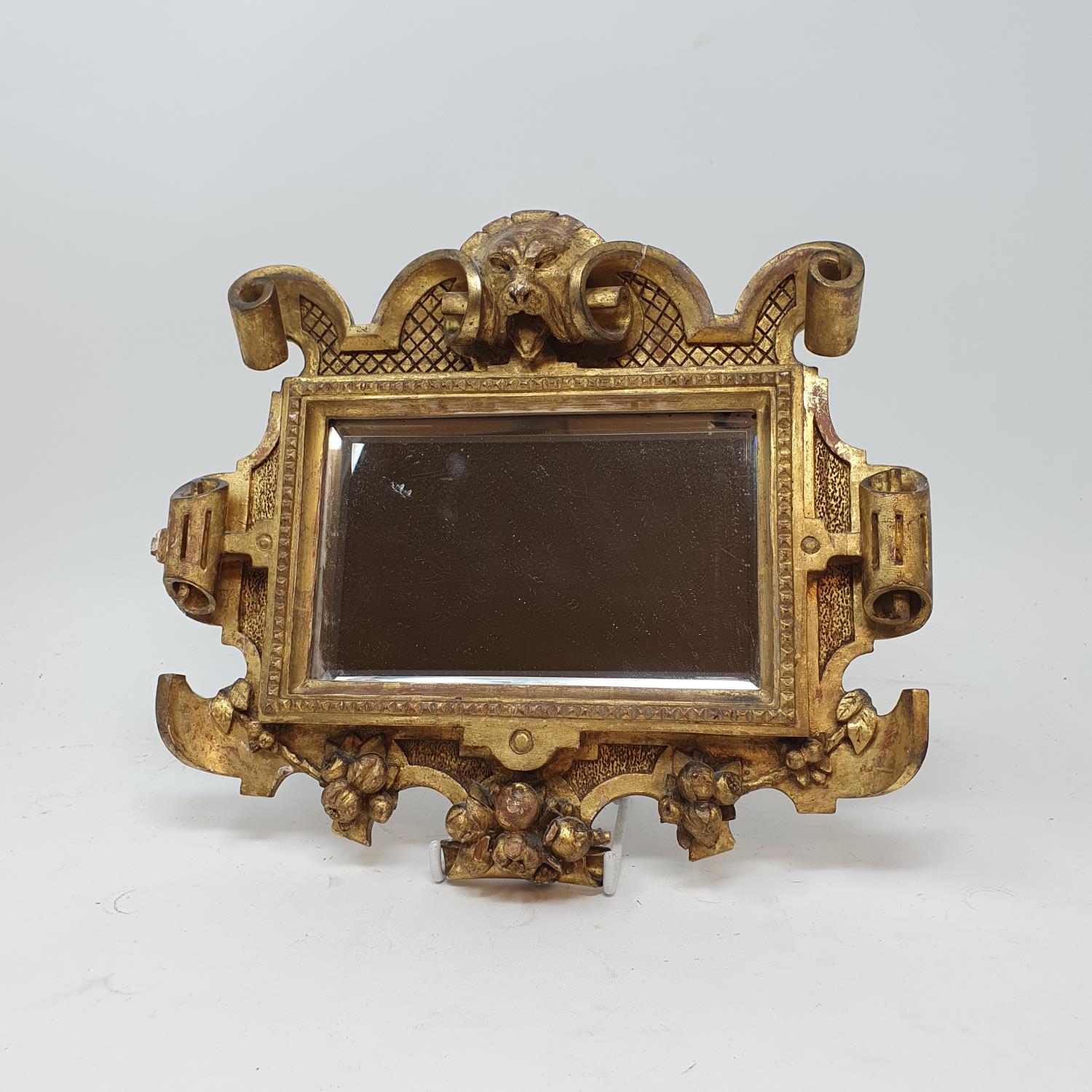 A carved wood and gilt mirror, with lion's head finial, 27 x 23 cm, a carved giltwood wall mount, 25