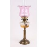 A Victorian brass oil lamp with clear glass reservoir and pink shade.