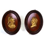 A pair of mahogany oval wall plaques, each decorated with a relief portrait of a classical figure,