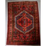 A Persian Hamadan hand knotted woollen rug with stylised design within borders, on a red ground,