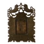 An Indian brass strut picture frame with engraved foliate decoration surmounted with a pair of