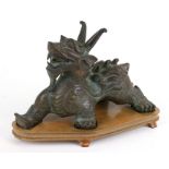 A large heavy Chinese bronze archaic style of a lion dragon, on a hardwood stand, 30cms (12ins)