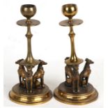 A pair of Regency style brass candlesticks, each surmounted with three cold painted bronze dogs,