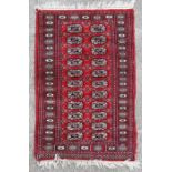 A Persian Turkoman woollen rug with repeated geometric designs within a multi border, on a red
