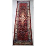 A Persian Hamadan hand knotted woollen runner with central motif within a stylised border on a red