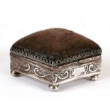 An Edwardian silver pin cushion of rectangular form with repeating wave scroll decoration, on bun