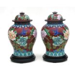 A large pair of Chinese cloisonne baluster vases on stands decorated with flowers on a deep red