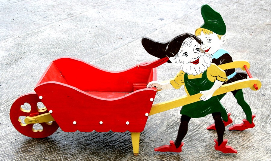 A novelty painted wooden wheelbarrow being pushed by two gnomes, 97cms (38ins) long.