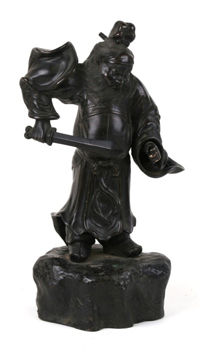 A Japanese bronze figure in the form of a warrior holding a sword, on a rocky base, 33cms (13ins)