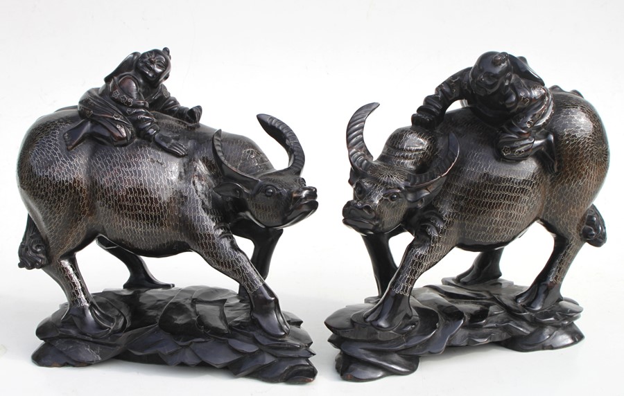 A pair of Chinese hardwood groups depicting children riding water buffalos, profusely inlaid with