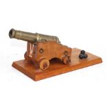 A desk top cannon with a brass barrel mounted on a wooden carriage with brass & metal fittings,