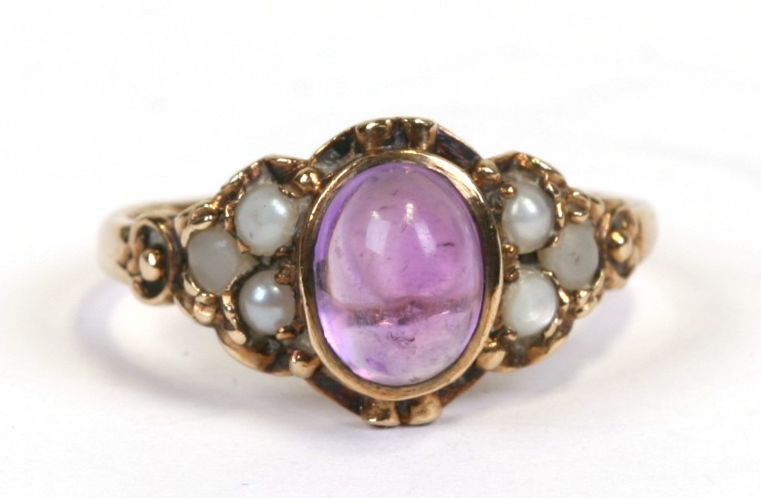 A 9ct gold ring set with a central amethyst cabochon flanked by seed pearls, approx UK size 'N'.