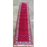 A Persian Tabriz woollen hand knotted runner with red ground within floral borders, signature to one
