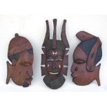 An African hardwood mask, 59cms (23ins) high; together with two African wall plaques (3).