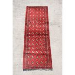 A Persian Balouch woollen hand knotted runner with repeat design on a red ground, 193 by 67cms (76