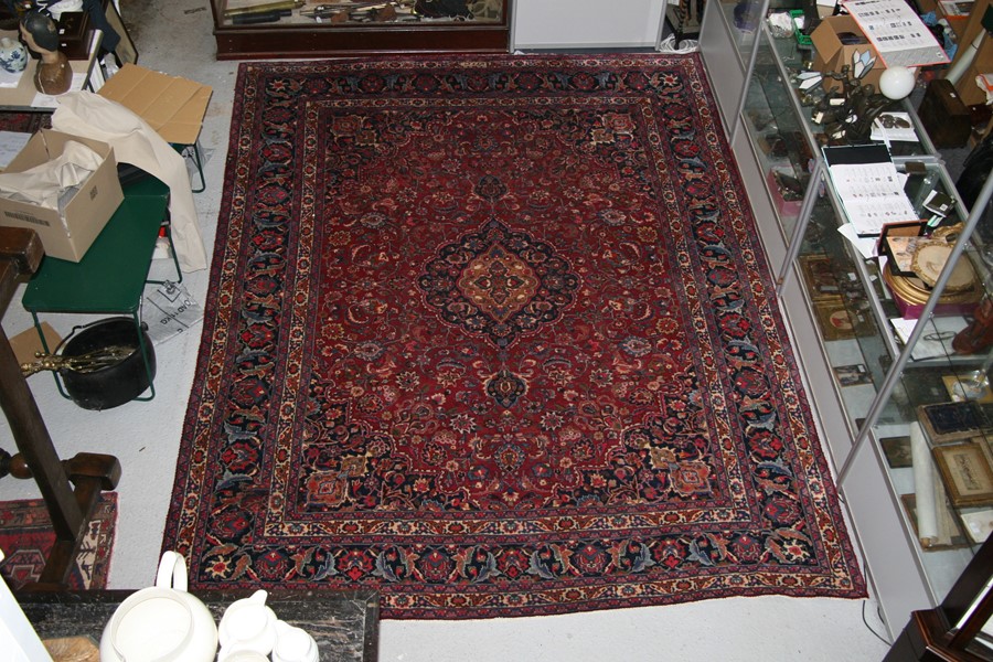 A Persian Kashan hand knotted woollen carpet with central floral gul within floral borders, on a red