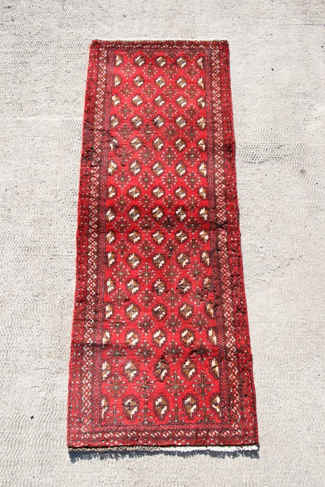 A Persian Balouch woollen hand knotted runner with repeat design on a red ground, 193 by 67cms (76