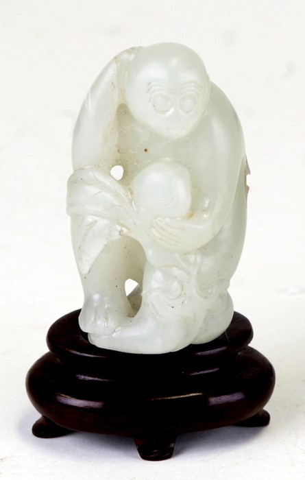 A Chinese jade figure in the form of a monkey holding a fruit, on an associated hardwood stand, 5cms