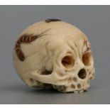 A Japanese ivory netsuke carved in the form of a skull with shibayama decoration, 3.5cms (1.25ins)