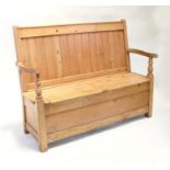A stripped pine settle, the seat divided into two sections with lift-up lids, 145cms (57ins) wide.
