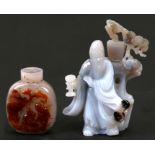 A Chinese carved agate figure depicting a robed man standing beside a tree, on a hardwood stand,