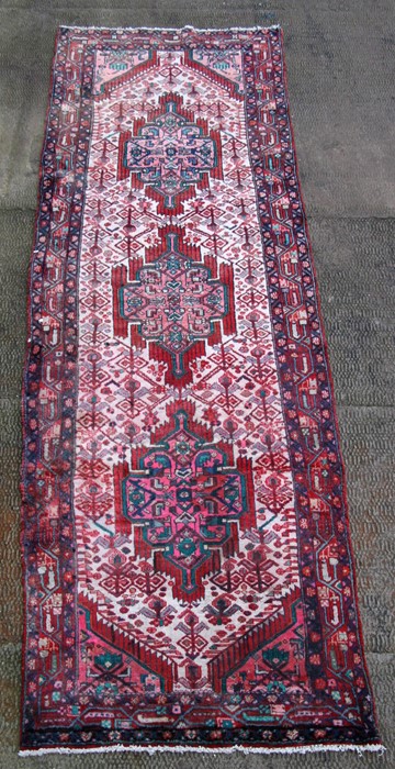 A Persian Hamedan woollen hand knotted runner with three repeated guls within stylised borders on