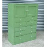 A green painted cupboard with twin panelled doors above an arrangement of seven drawers with glass