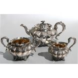 A William IV silver three-piece tea set of circular melon repousse form, with acanthus and flower