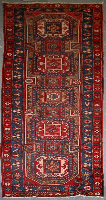 A Persian Azari hand knotted woollen runner with five stylised guls within floral borders, on a blue