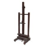 An early 20th century oak adjustable easel, the adjustable rack standing on four casters, 62cms