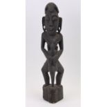 An African carved wooden ebonised standing figure holding a log, 50cms high.