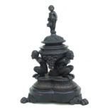 A 19th century bronze inkwell and cover, the cover surmounted with a cherub, the well supported by
