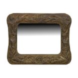 An embossed brass framed wall mirror decorated with scrolling flowers with central letter 'G' and