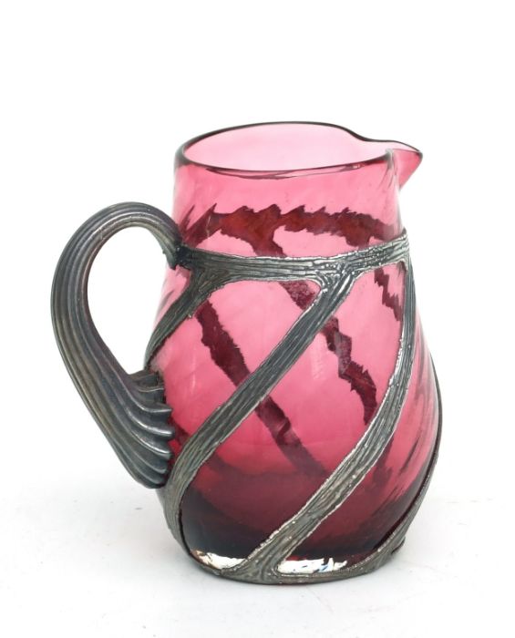 A cranberry cream jug with white metal overlay decoration, 9.5cms high.