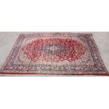 A Persian rug with central medallion within a foliate scrolling border, on a red ground, 300 by