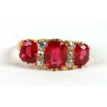 A yellow metal (tests as gold) ring set with three large red stones interspersed with diamonds,