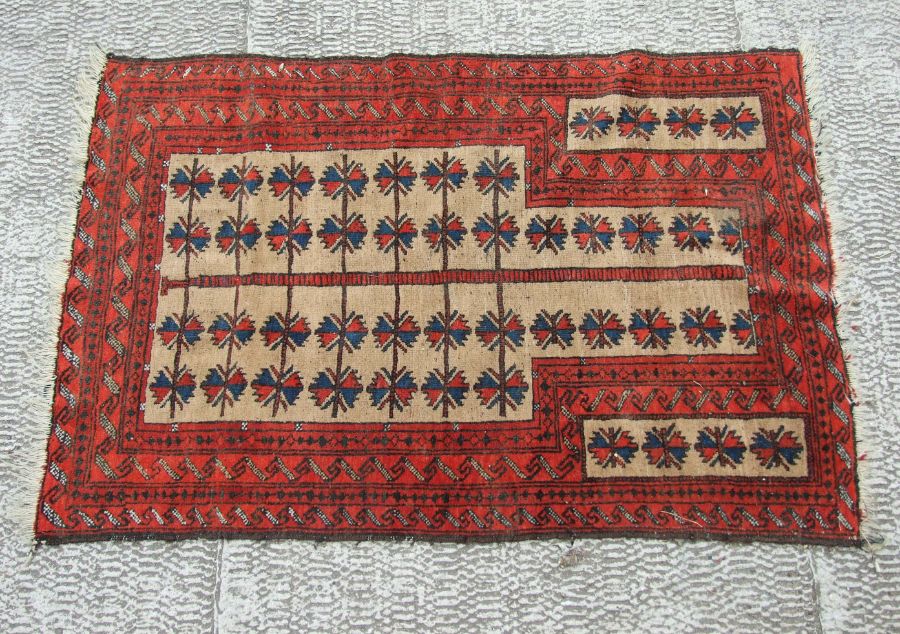 A Persian Baluch woollen hand knotted prayer rug with repeating motifs on a red ground, 84 by