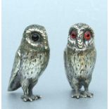 A matched pair of silver coloured metal pepperette in the form of owls with glass eyes, weight