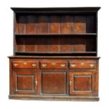 An 18th century oak dresser, the moulded cornice above a plate rack, with panelled cupboards and