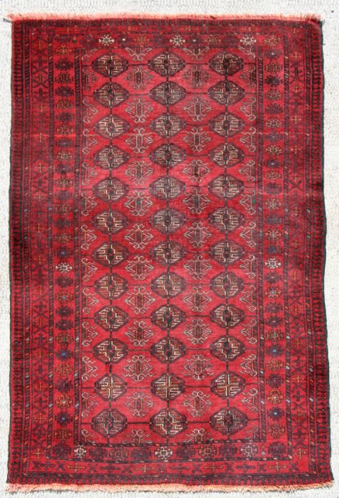 A Persian Balouch rug with repeat design on a red ground, 202 by 115cms.