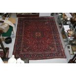 A Persian Kashan hand knotted woollen carpet with central floral gul within floral borders, on a red