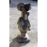 A well weathered reconstituted stone figure of a cherub playing a tambourine, seated on a column,