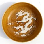 A Chinese footed shallow dish decorated in relief with a dragon chasing a flaming pearl, on a café