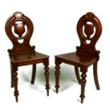A pair of Victorian mahogany hall chairs with pierced back splats and solid seats, on turned front