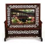 A Chinese hardwood table stand with pierced carved decoration and embroidered central panel