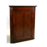 A 19th century oak hanging corner cabinet with single panelled door enclosing a shelved interior,