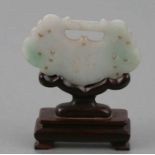 A Chinese carved jade buckle decorated with dragons on a carved wooden stand.
