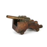 A brass table cannon, 14cms long, on a mahogany carriage with farthing wheels.